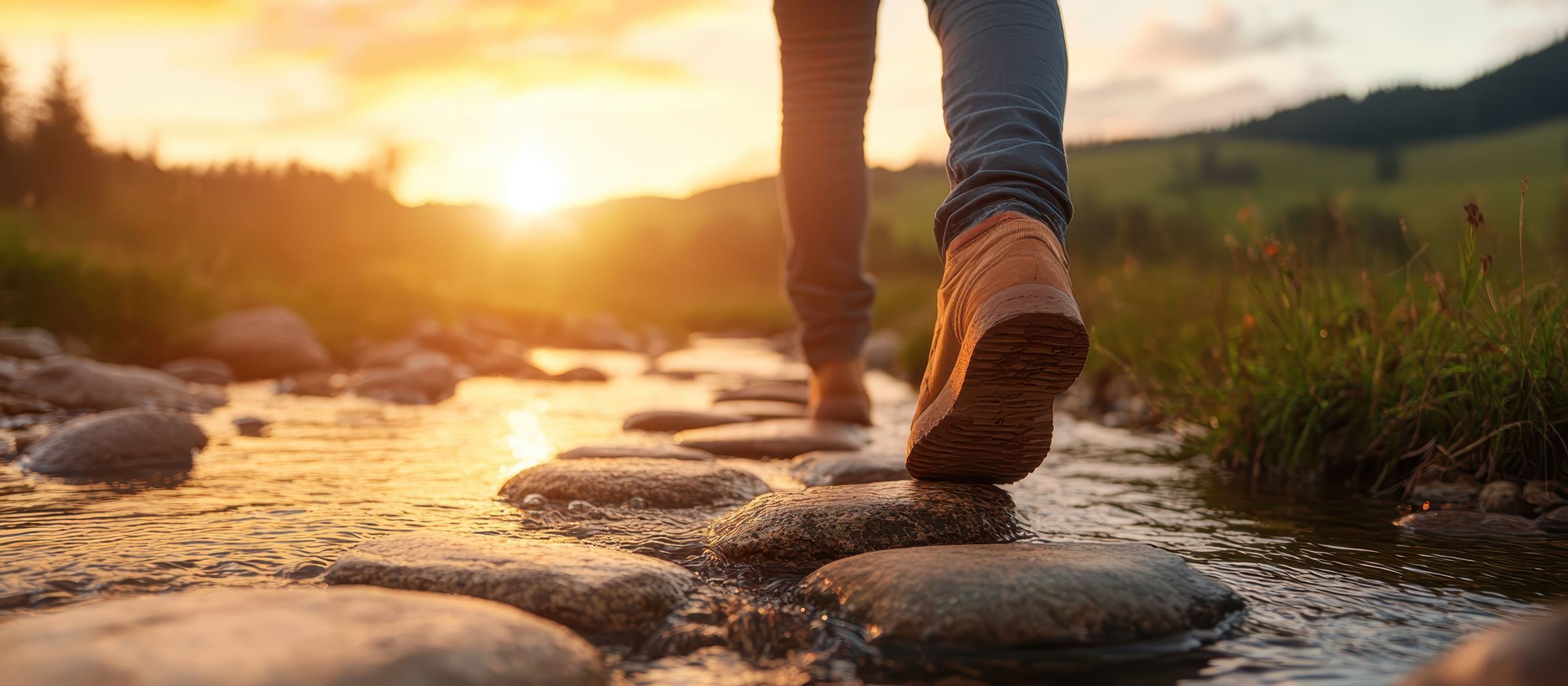 A person stepping from stone to stone across a stream at sunrise